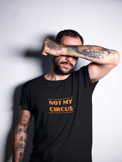 An attractive tattooed male, with his arm across his face to cover his eyes, wearing a black organic cotton unisex t-shirt with the slogan 'not my circus' written in bright orange across the chest.