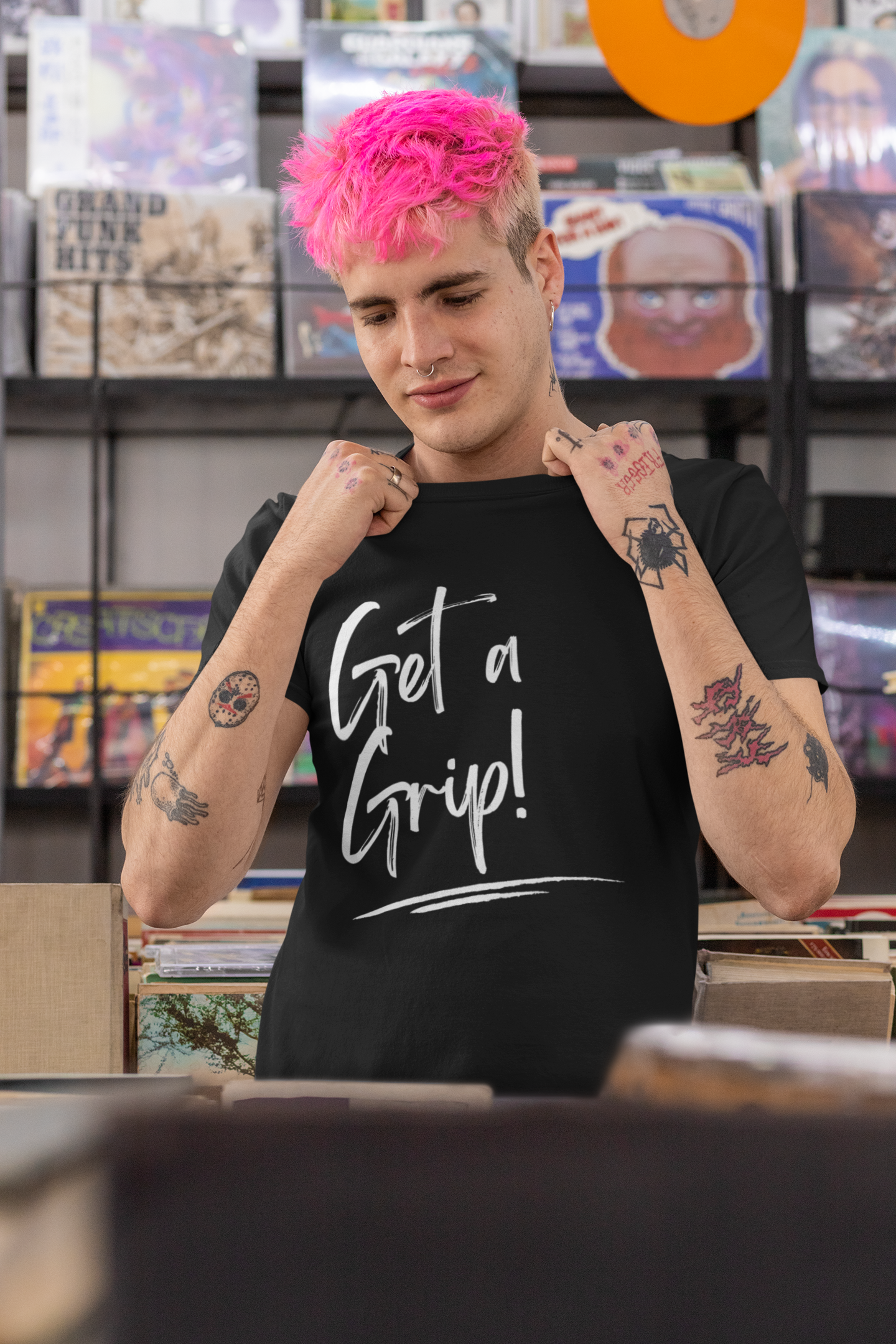 A young tattooed male with pink hair wearing a black organic cotton unisex t-shirt with the words Get a Grip! written across the chest in white.