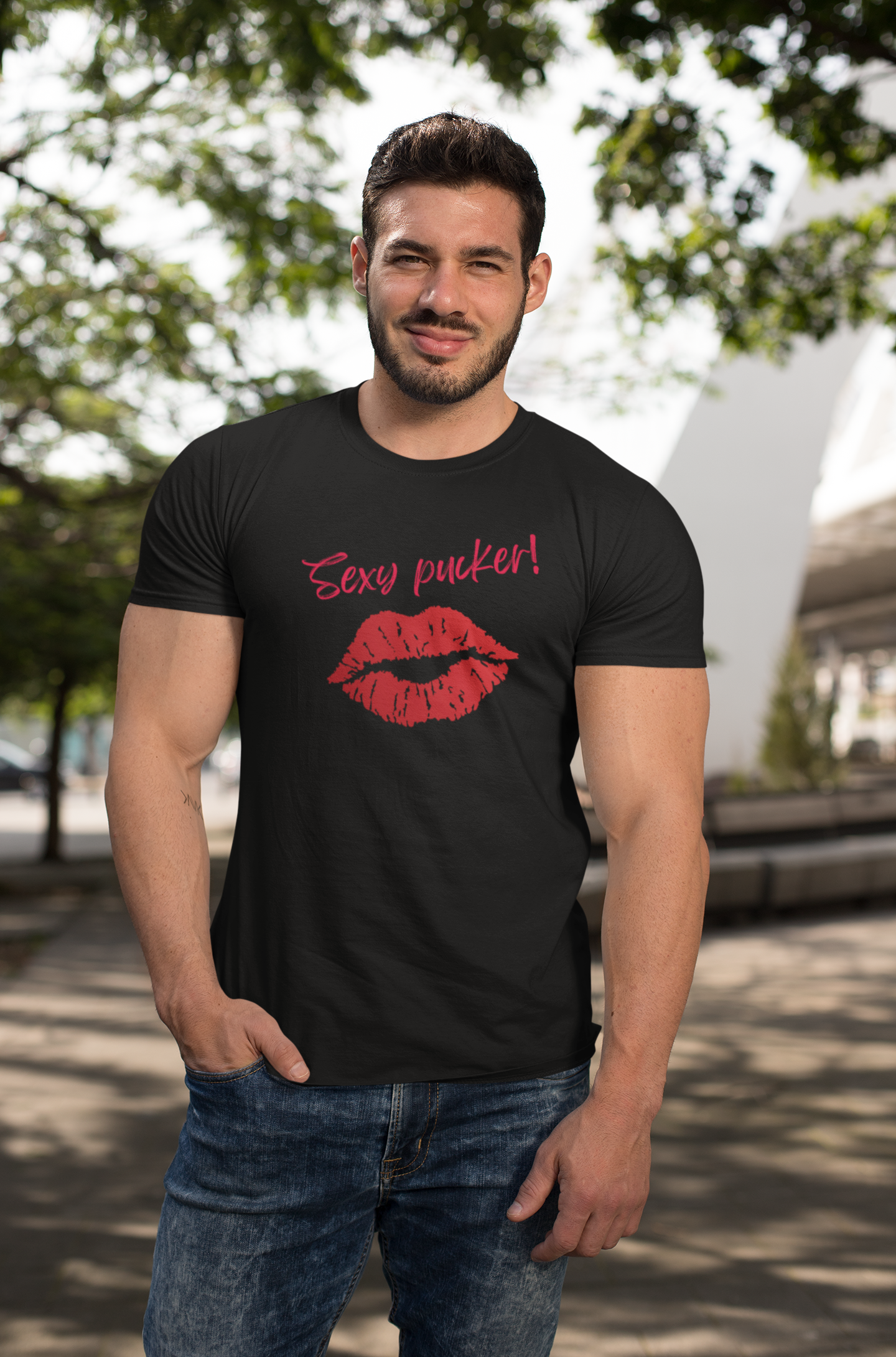 A muscular man stood wearing a tight black organic cotton unisex t-shirt with bright red lips and the words 'Sexy pucker!' on the chest.